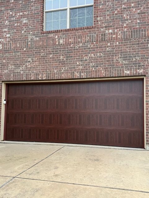 Closed dark brown garage door on a brick building with a concrete driveway and window above.