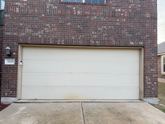 Closed white garage door in a brick building with a concrete driveway in front