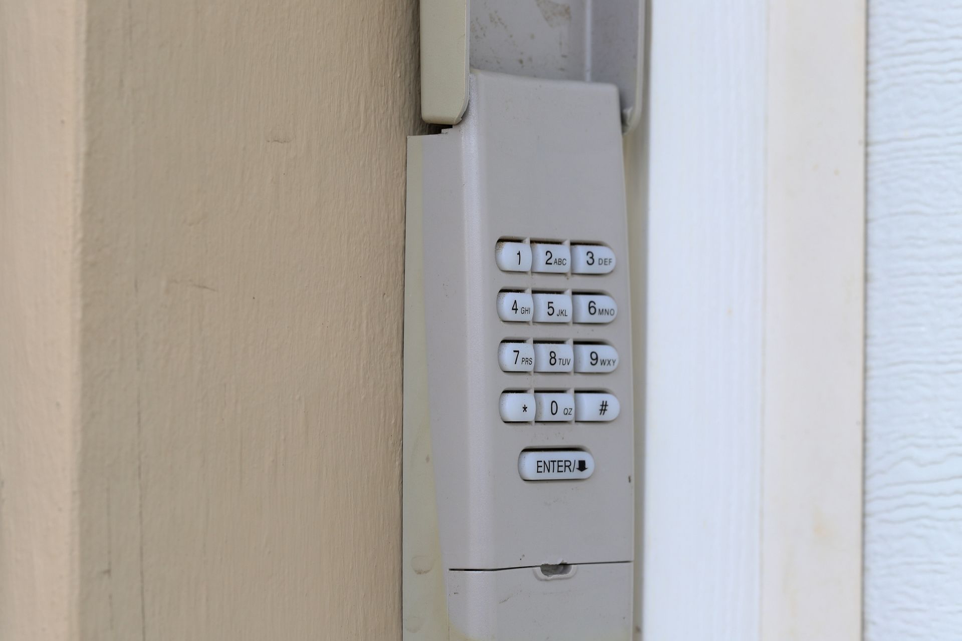 White wall-mounted keypad lock beside a beige door frame and white wall.