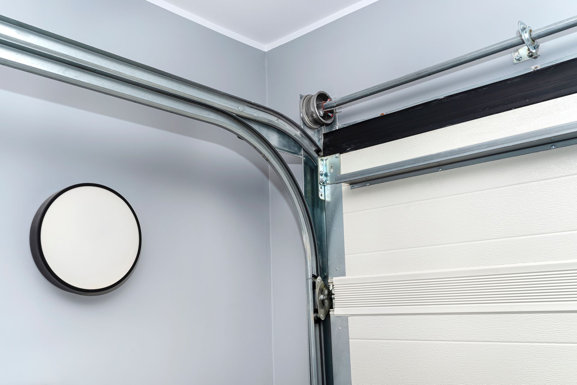 Garage door corner with metal track, spring, and beige blind on a gray wall