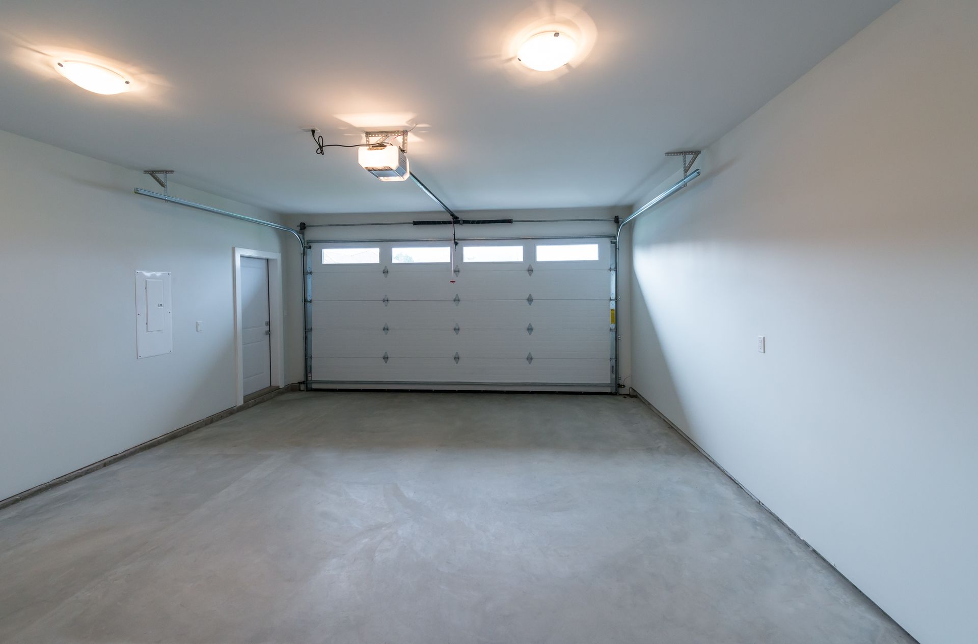 Empty white garage with closed door, concrete floor, and ceiling lights