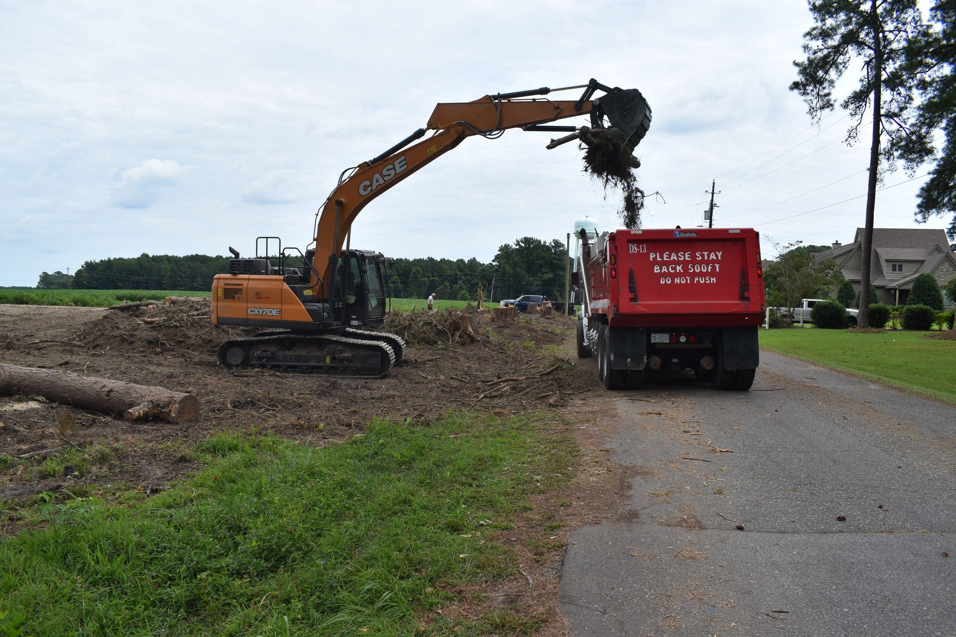 Excavator loading dirt into a red dump truck beside a roadside work site