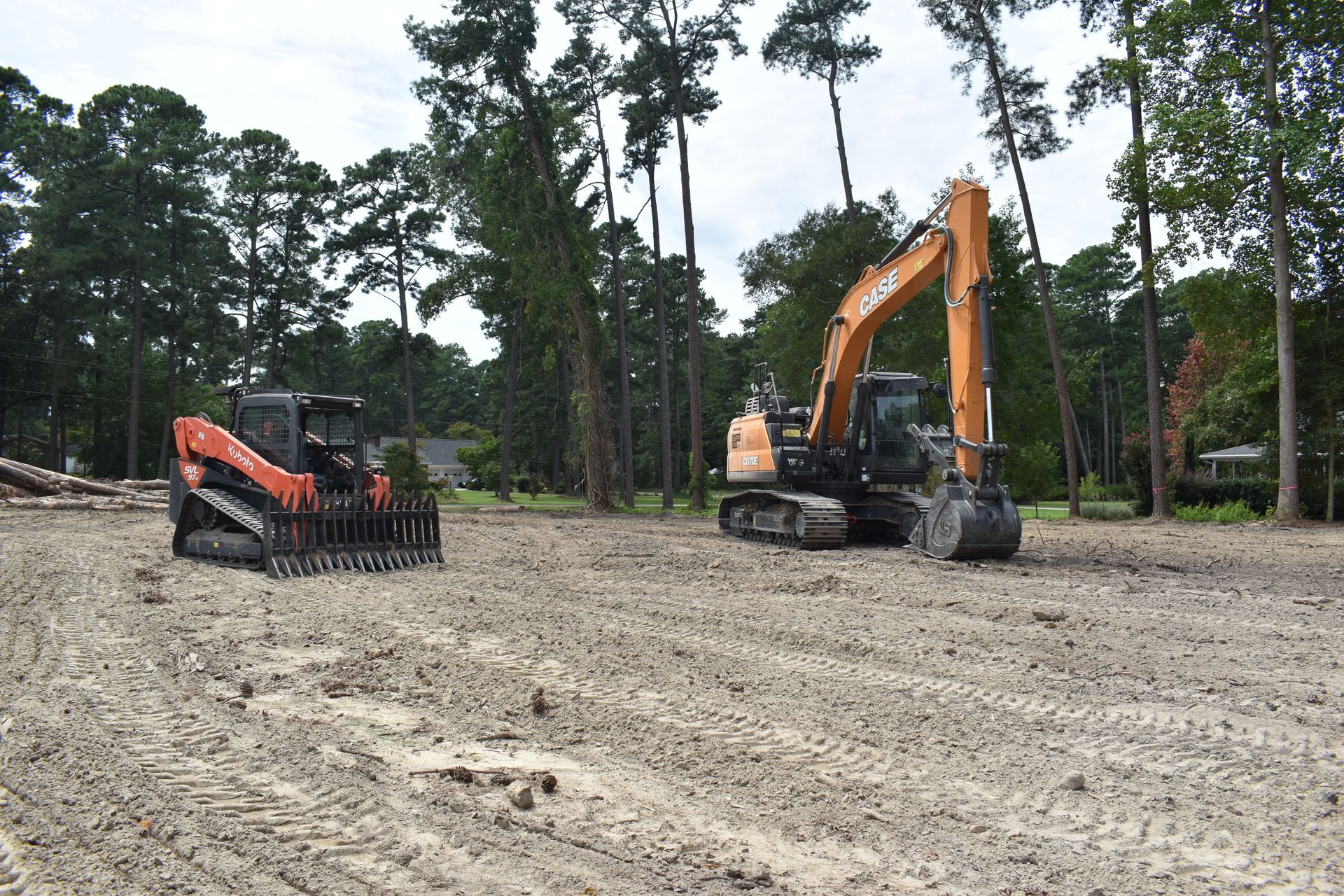 Orange excavator loading dirt into a red dump truck at a muddy construction site with logs in the foreground