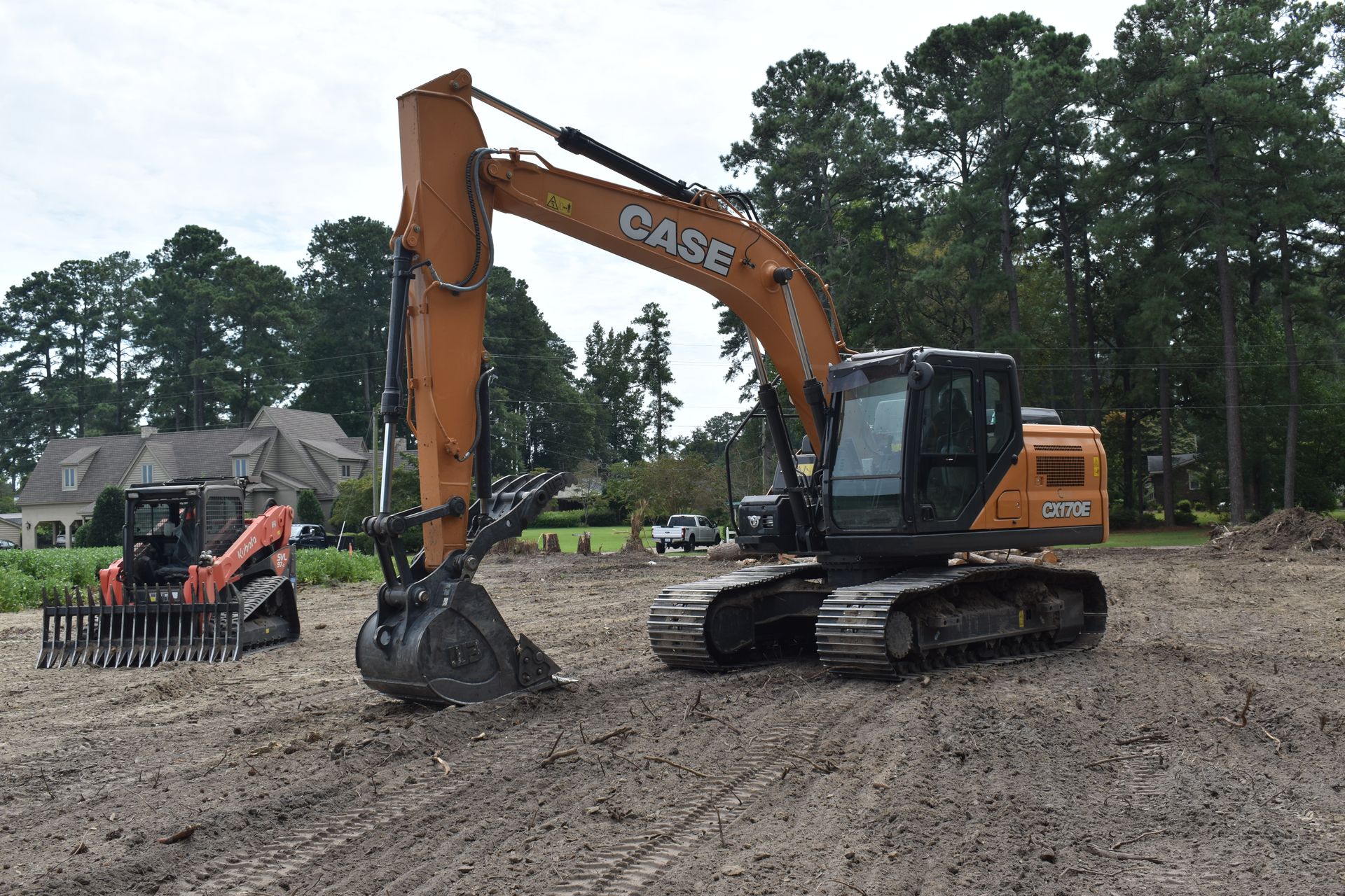 Orange CASE excavator working on a muddy construction site beside a small tractor.