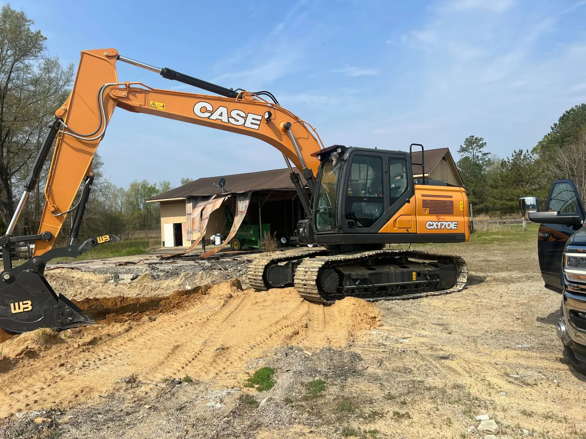 Orange CASE excavator on a dirt lot beside a damaged building, with debris in the foreground.