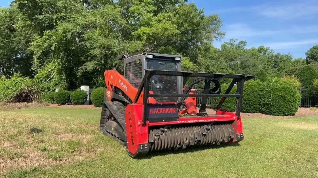 Red skid steer mower on grass field with trees in the background