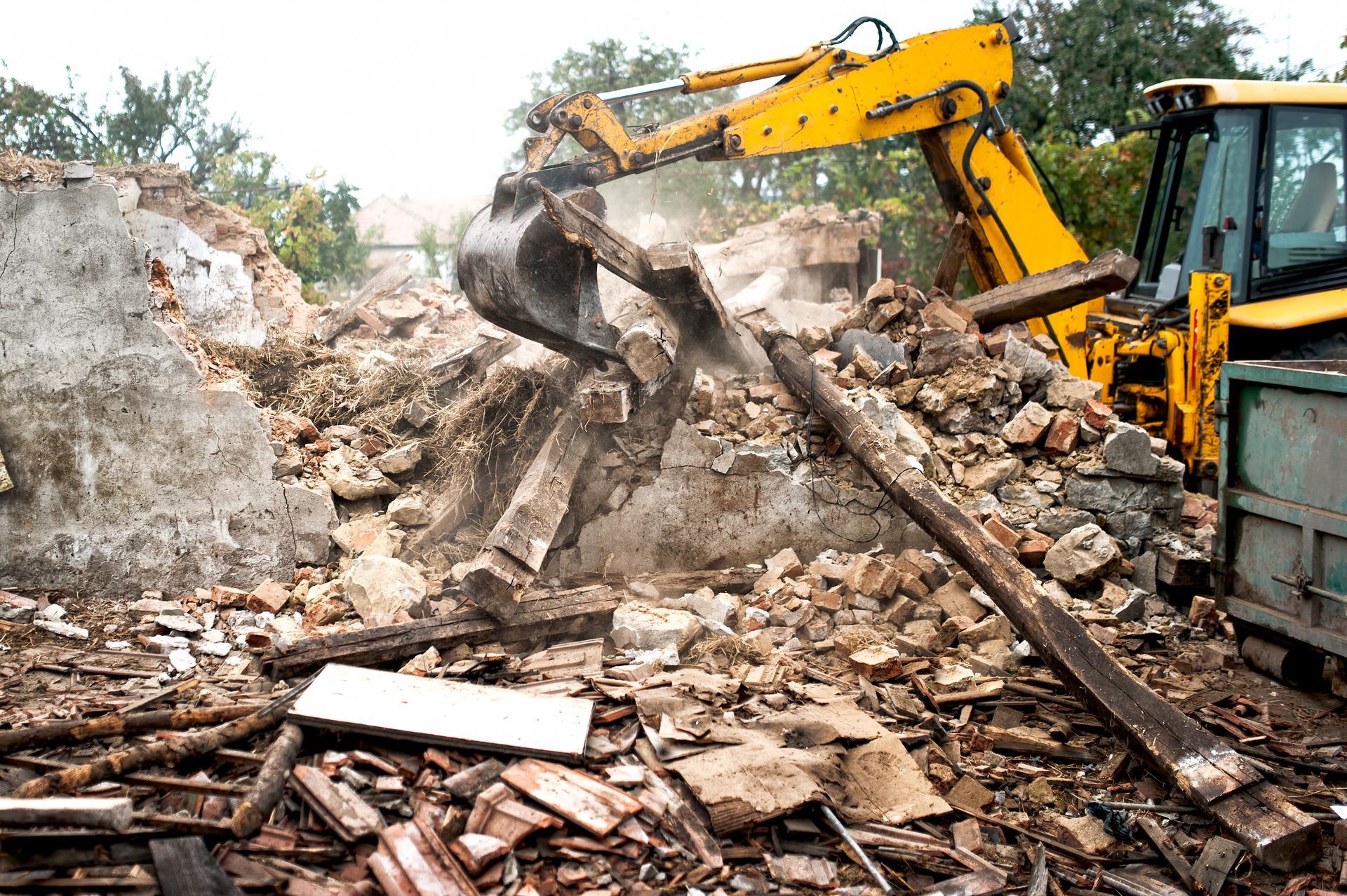 Yellow excavator demolishing rubble at a construction site, lifting debris amid dust.