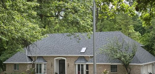A white house with a black roof is surrounded by trees and leaves.