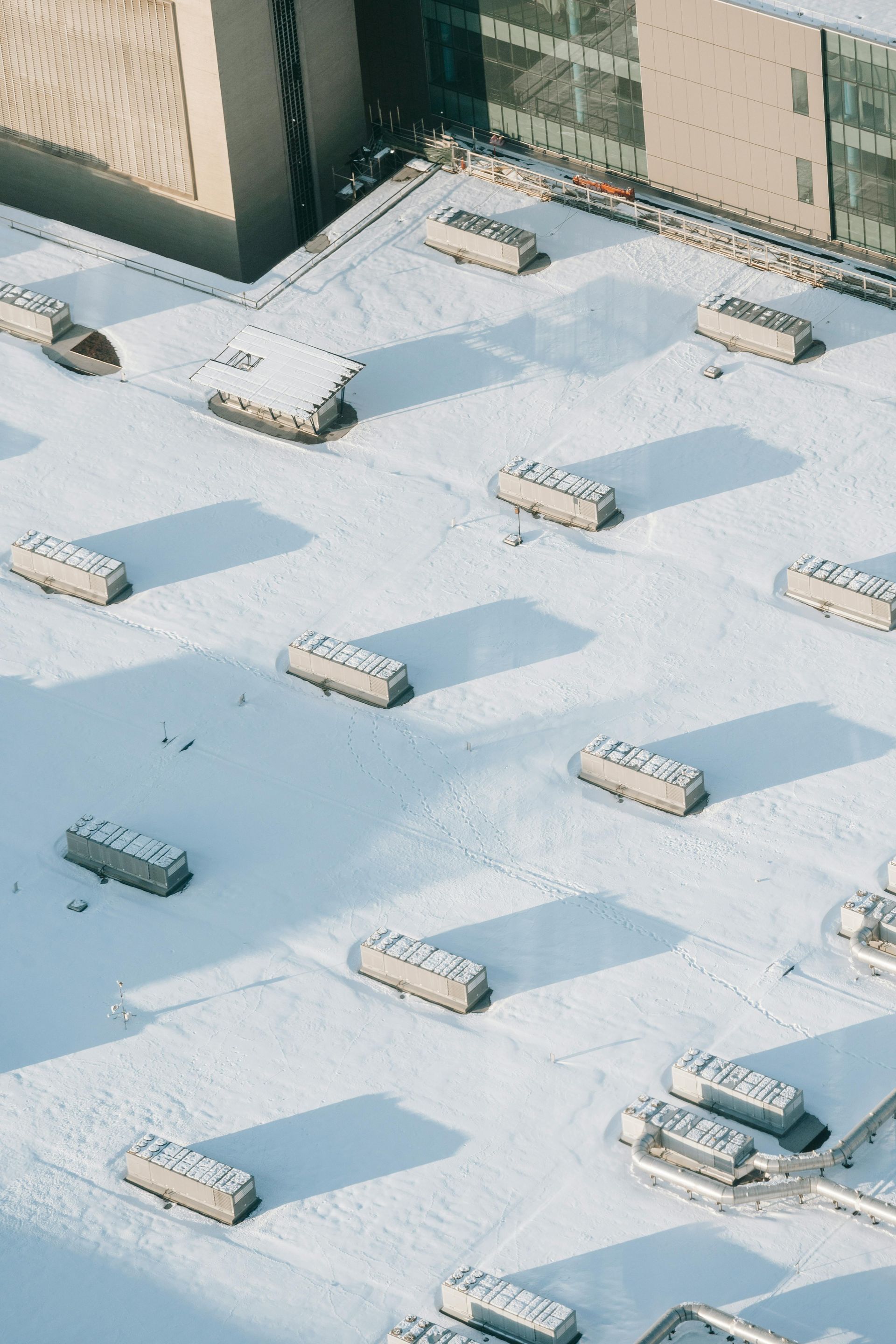 Snow-covered rooftop with several rectangular HVAC units casting long shadows.