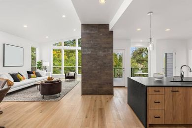Open-concept living space with kitchen and living room. Wooden floors, white walls, and a large central dark accent wall.
