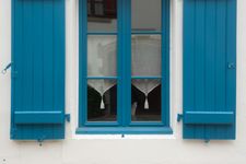Blue window shutters flank a blue-framed window with white curtains.
