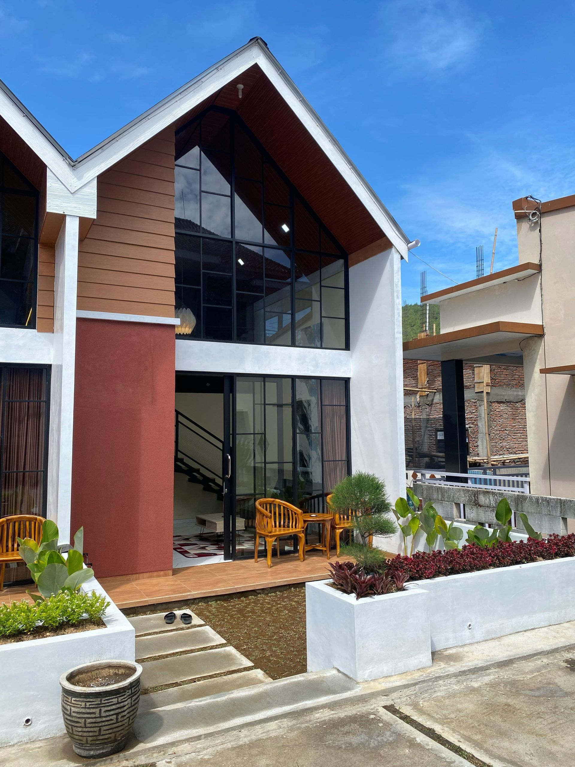 Two-story modern home with large windows, brown and white facade, and small garden.