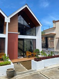 Modern two-story house with red and white facade, large windows, and manicured landscaping under a blue sky.
