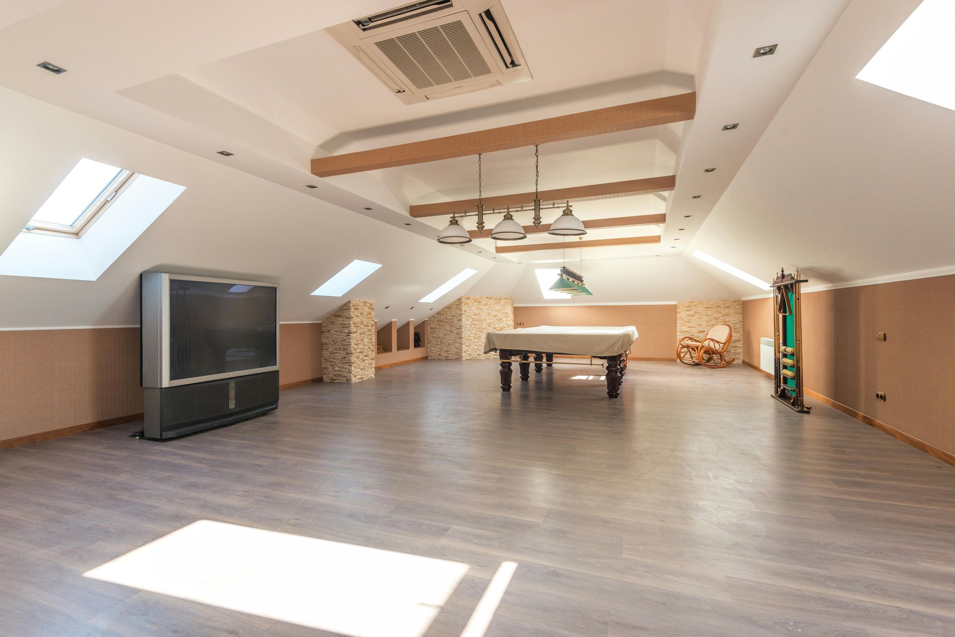 Spacious attic room with a pool table, large TV, skylights, and exposed beams.