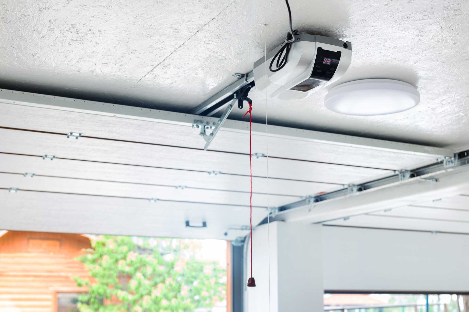Garage door opener mounted on a ceiling track, with a red pull cord hanging down.
