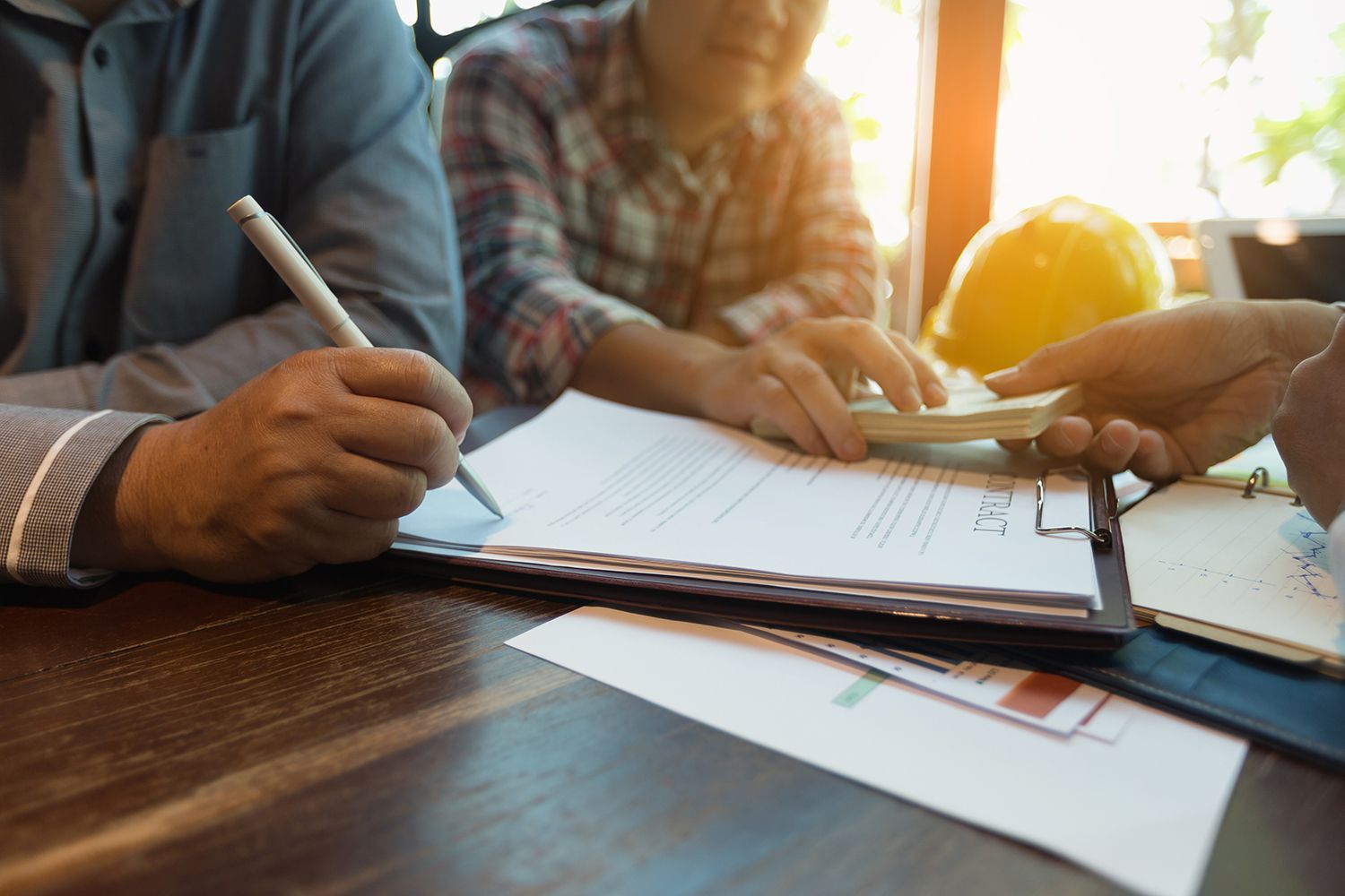 People signing documents at a sunlit office table with a clipboard and papers People signing documents at a sunlit office table with a clipboard and papers