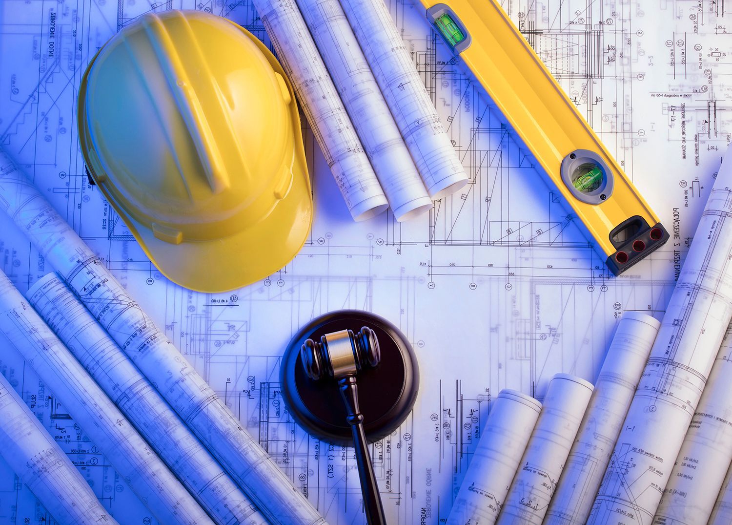 Yellow hard hat, blueprints, rolled plans, and a measuring tape arranged on a construction drawing. Yellow hard hat, blueprints, rolled plans, and a measuring tape arranged on a construction drawing.
