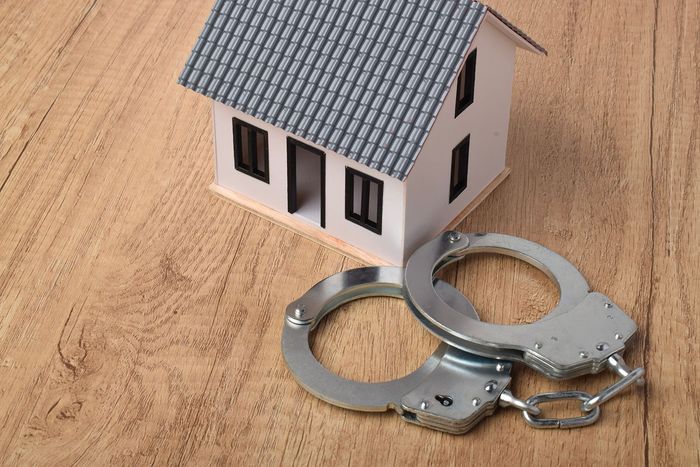 Two metal handcuffs beside a small model house on a wooden surface