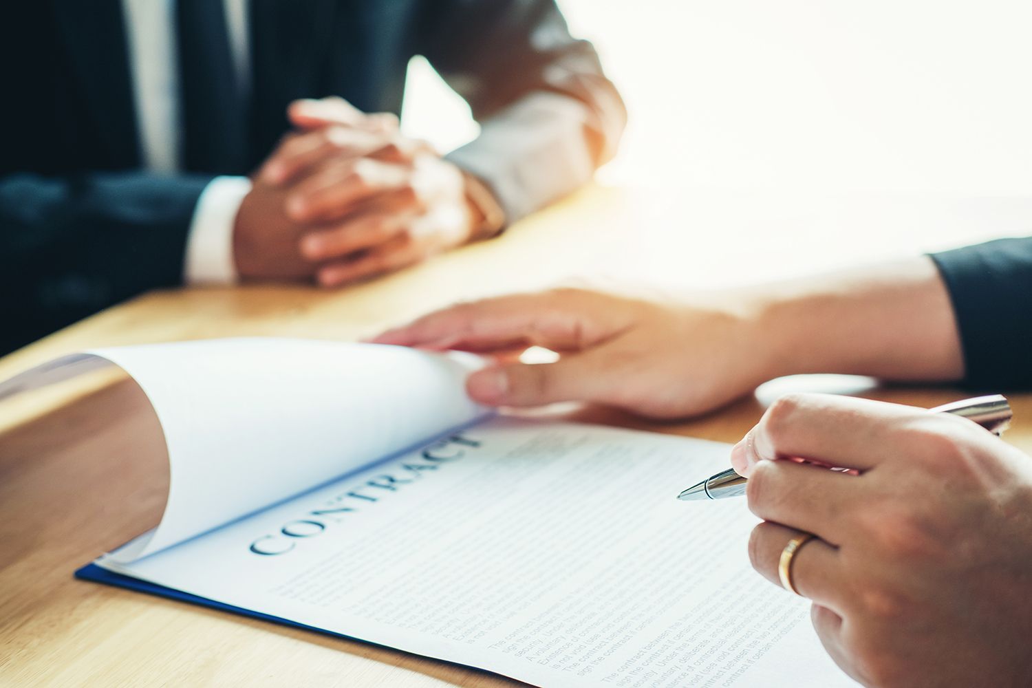 Hands reviewing and signing a contract on a desk with a pen and document. Hands reviewing and signing a contract on a desk with a pen and document.