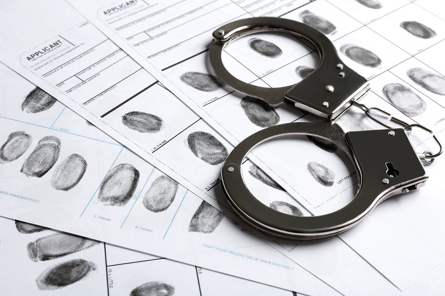 Handcuffs on fingerprint forms, suggesting a crime scene or forensic investigation Handcuffs on fingerprint forms, suggesting a crime scene or forensic investigation