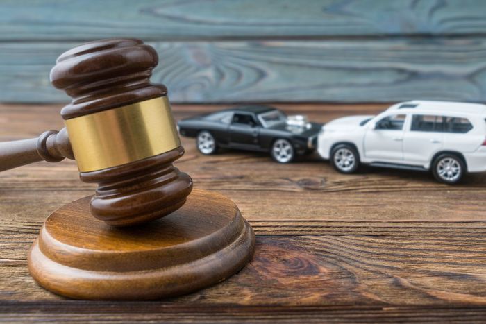 Gavel on wooden desk with two parked cars in the background, suggesting a legal auto case