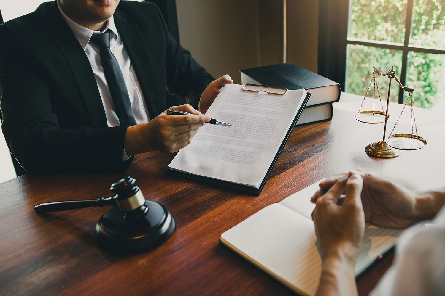 Lawyer discussing a case at a desk with documents, gavel, and scales by a window