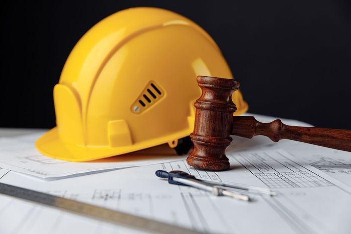 Yellow hard hat and judge’s gavel on paperwork, symbolizing workplace safety and legal issues
