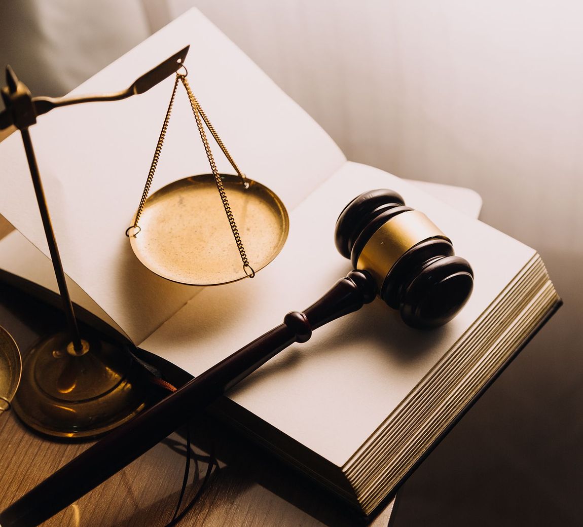 Law scales and gavel resting on open legal book, warm-toned courtroom concept