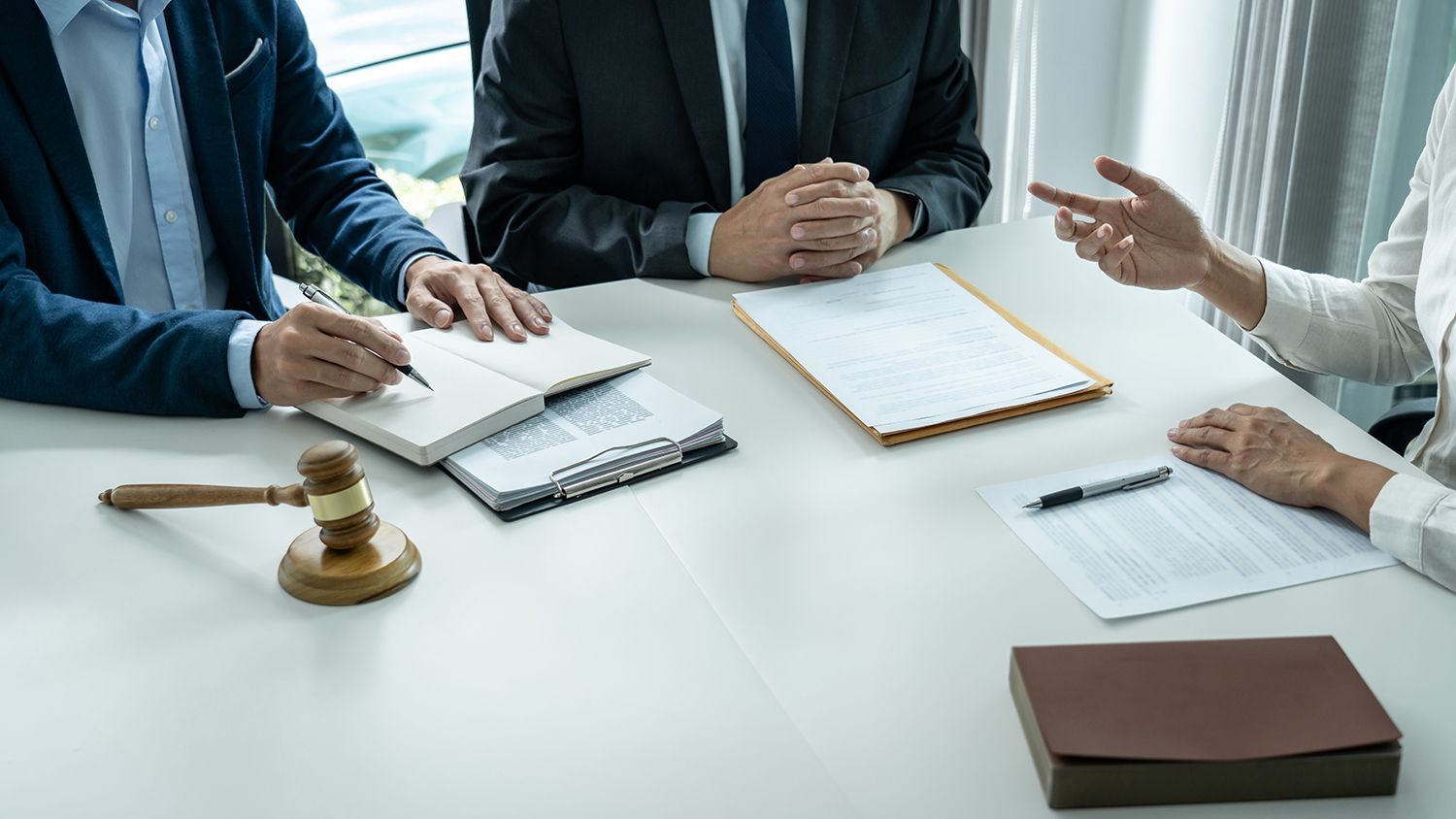 Business meeting with people signing documents at a white conference table, with a gavel and folder nearby