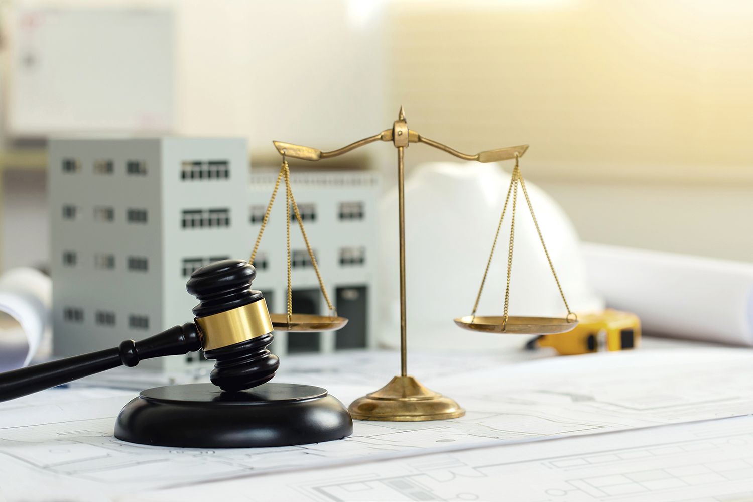 Lawyer’s gavel and scales on desk with courthouse model in background Lawyer’s gavel and scales on desk with courthouse model in background