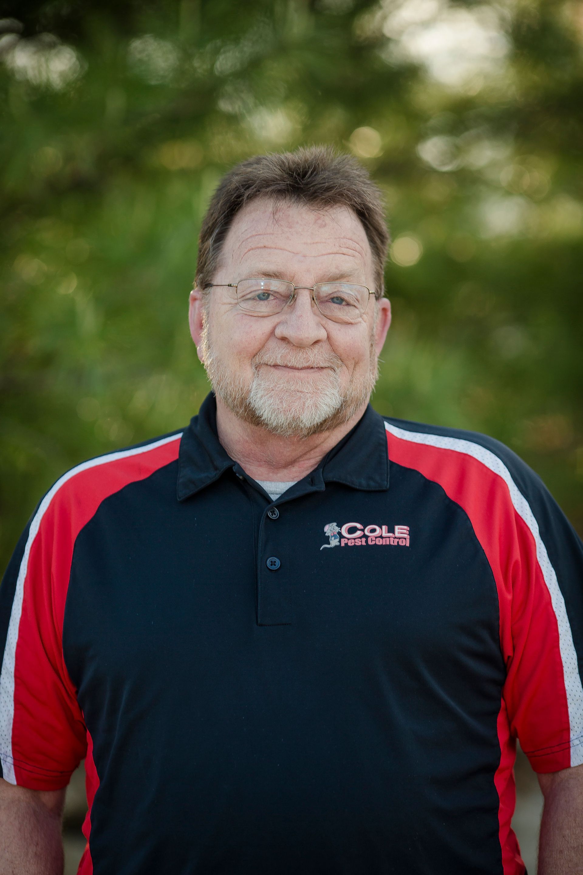 Smiling man in a black polo with red sleeves standing outdoors against a blurred green background