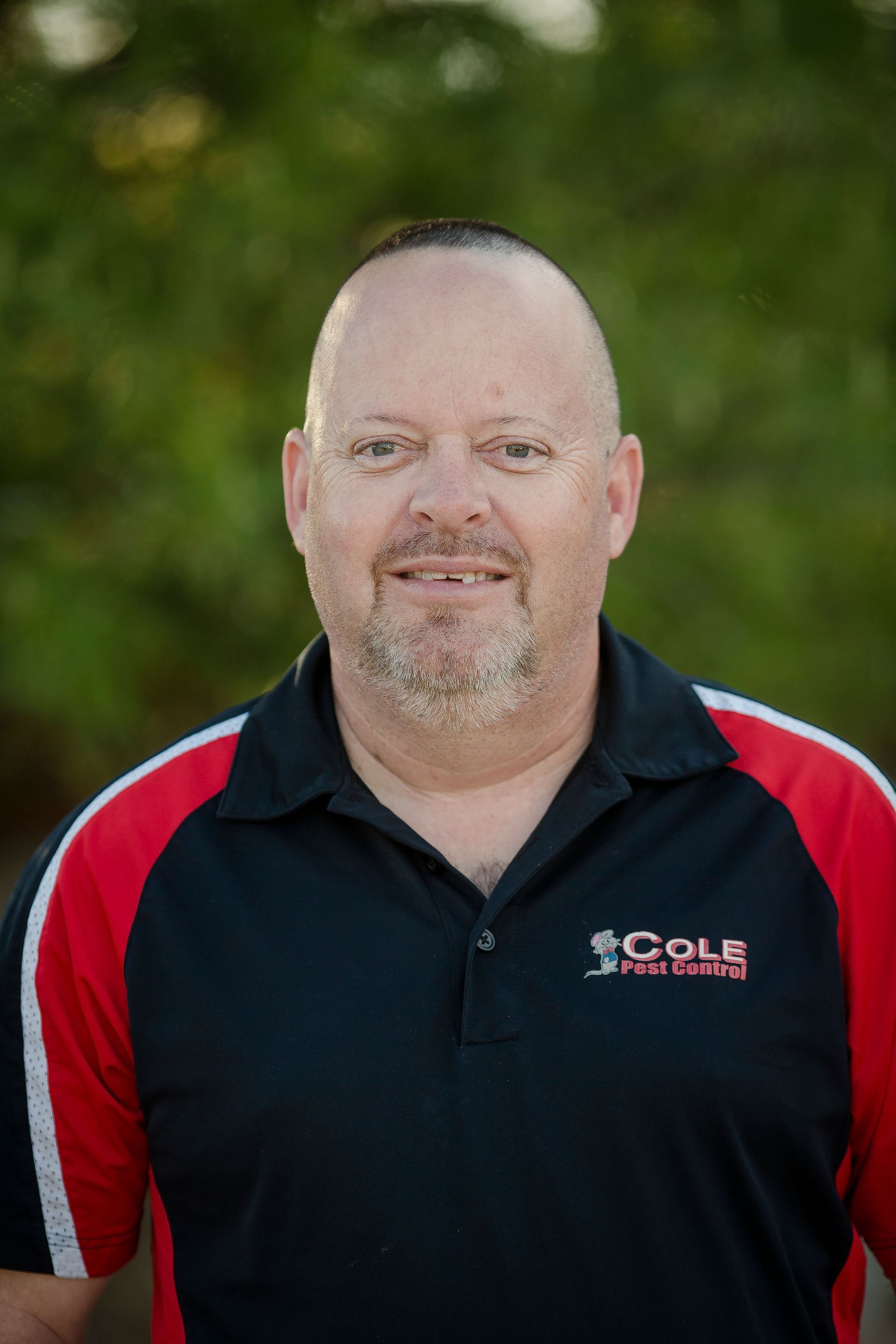 Man in black and red polo shirt standing outdoors against a blurred green background