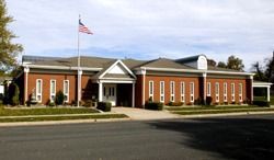Brick civic building with white columns and American flag in front, seen from the street