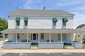 Two-story white house with green awnings and a covered front porch under a blue sky