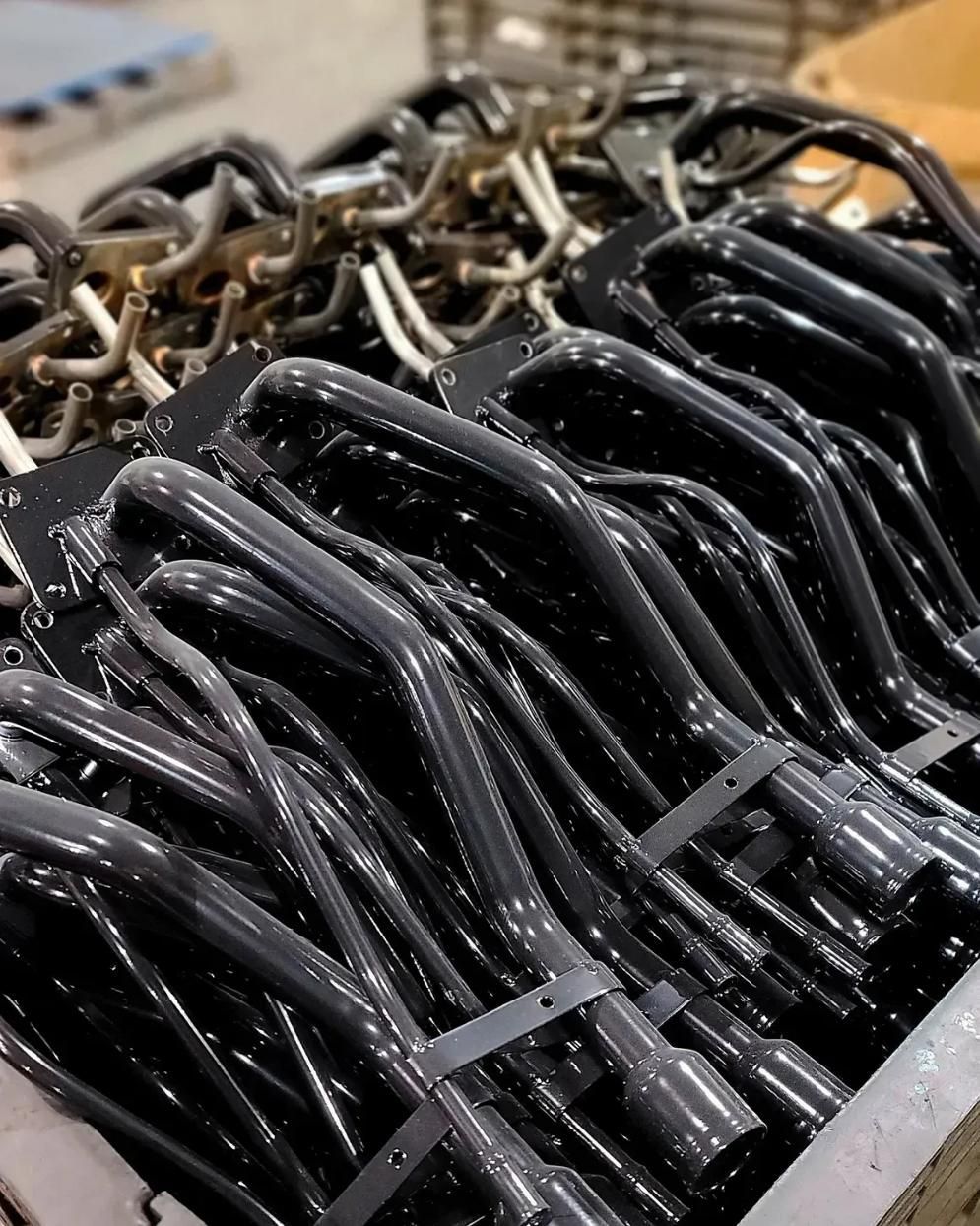 A bin filled with rows of new, black-coated industrial burner components stacked neatly for manufacturing.