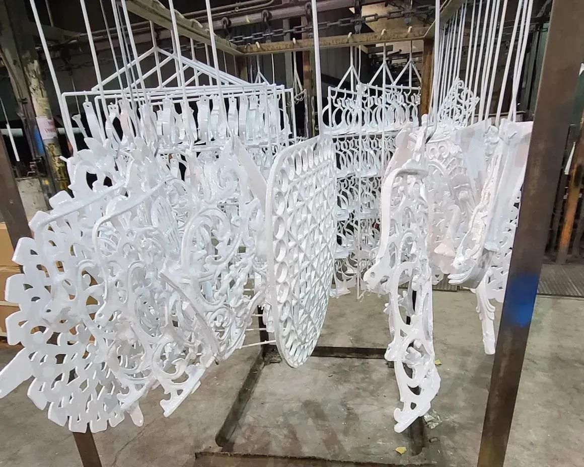 A row of ornate, white-painted metal pieces hangs from a rack in an industrial factory setting.