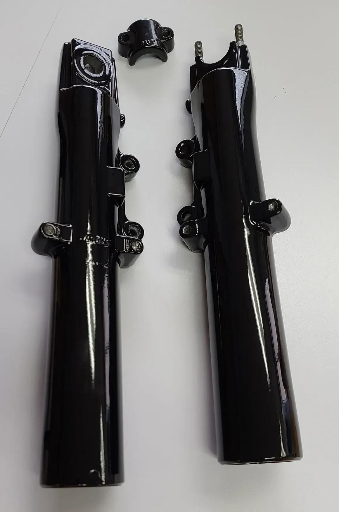 Two black metal motorcycle fork lower legs and a small black mounting bracket arranged on a white surface.