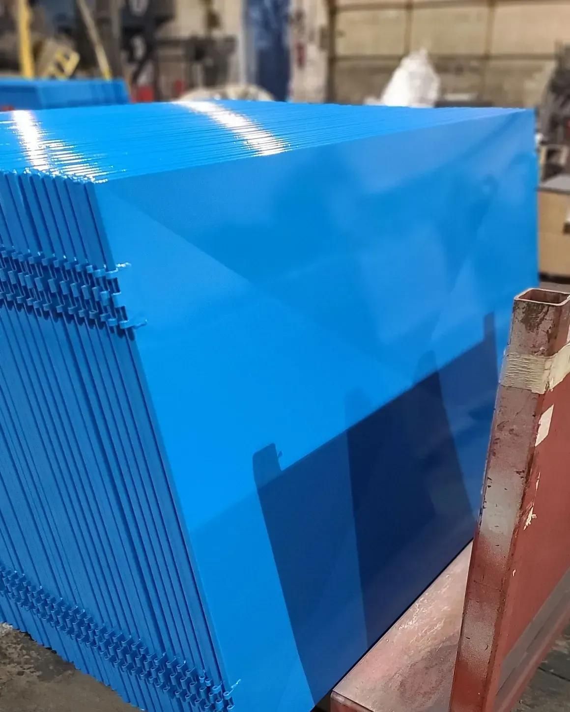 A stack of freshly painted, bright blue rectangular metal panels resting on a wooden pallet in an industrial workshop.