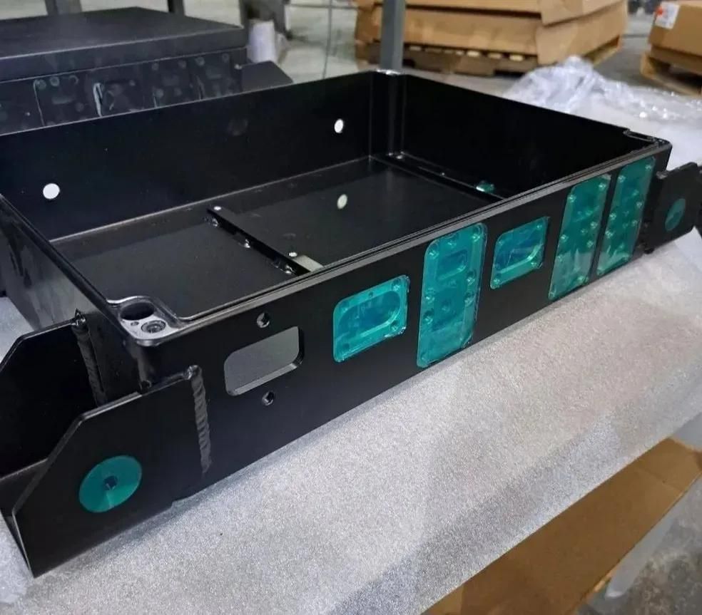 A black rectangular metal housing unit with several teal-colored protective tape patches, resting on a flat surface.