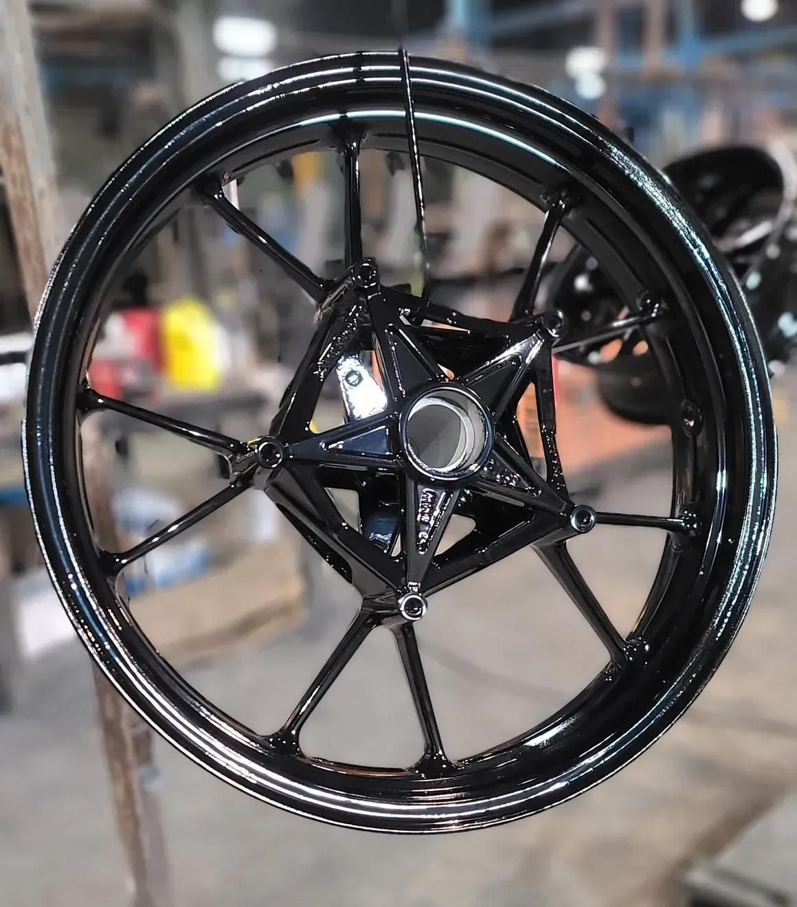 A glossy black motorcycle wheel with a five-spoke design, hanging in a workshop setting.