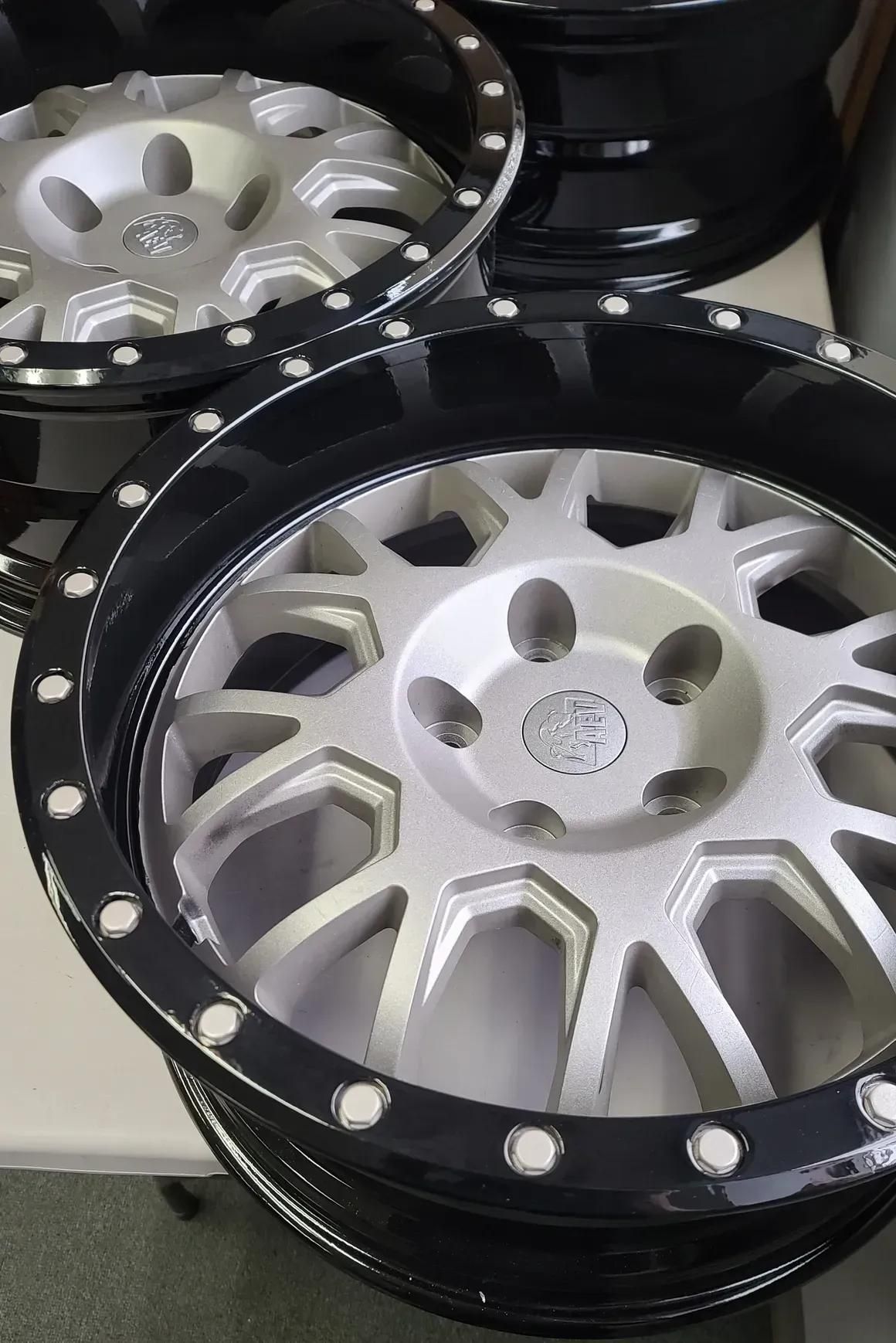 Two glossy black and silver off-road truck wheels with a multi-spoke design and simulated beadlock rim.