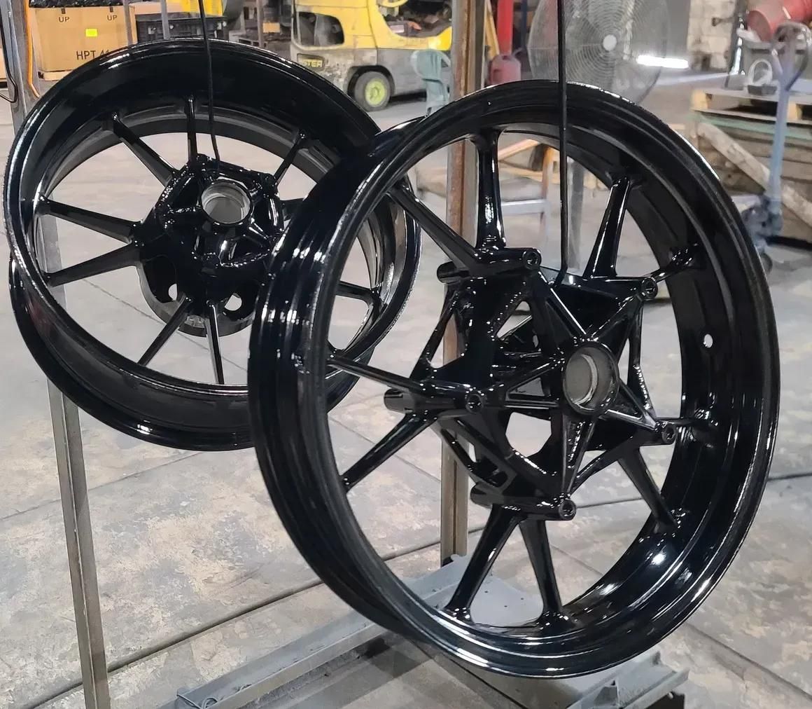 Two glossy black motorcycle wheels suspended on a metal rack in an industrial workshop.