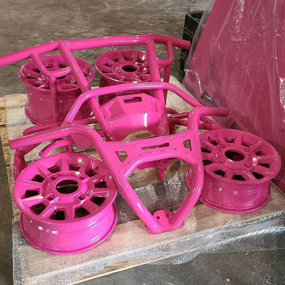 Bright pink powder-coated vehicle wheels and metal structural components resting on a pallet in a warehouse.