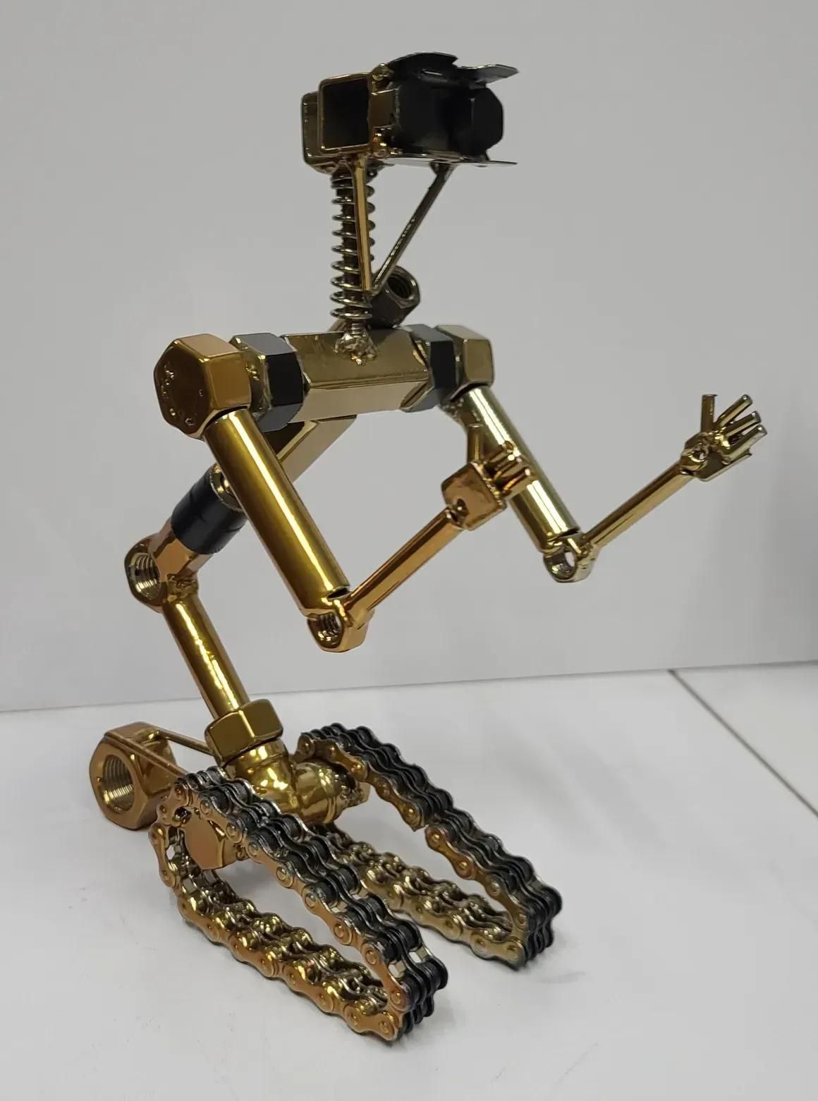 A steampunk-style sculpture of a robot made of gold-colored hardware, nuts, and chains, posing with arms raised.