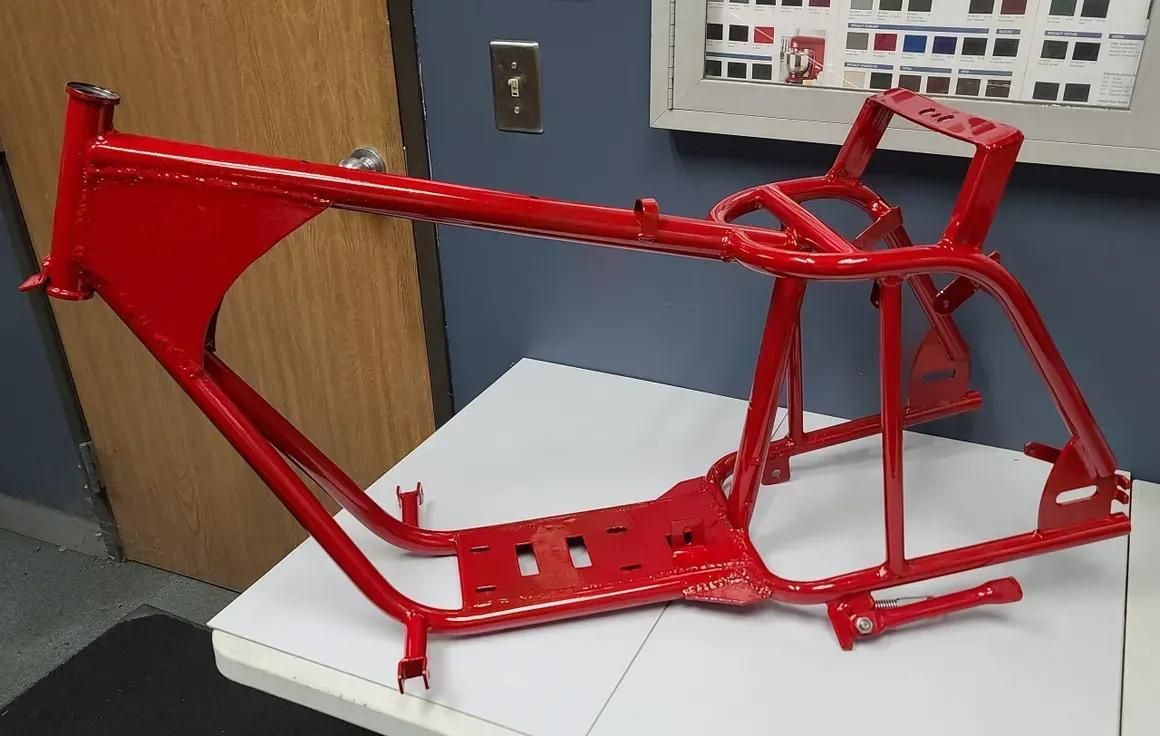 A bright red, freshly powder-coated metal motorcycle frame sitting on a white table.
