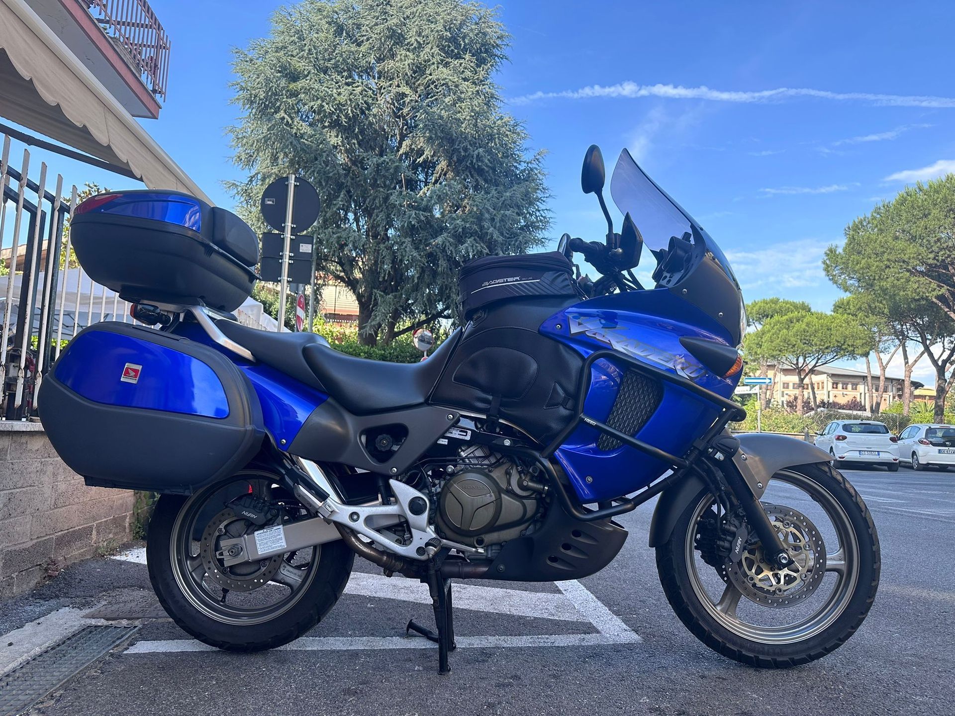 Motocicletta da turismo blu parcheggiata in strada sotto un cielo azzurro brillante, con borse laterali posteriori.
