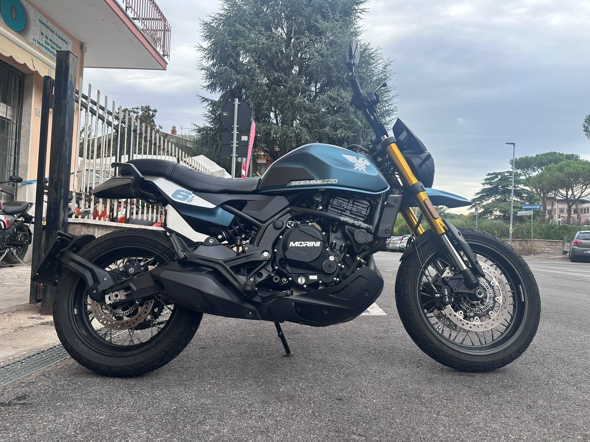 Una motocicletta sportiva nera parcheggiata sul marciapiede davanti a un edificio, sotto un cielo nuvoloso.
