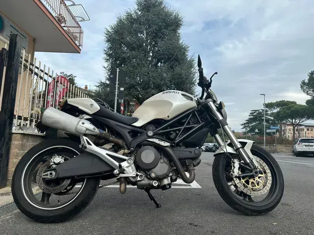 Una motocicletta Ducati Monster bianca parcheggiata all'aperto su una superficie asfaltata sotto un cielo nuvoloso.