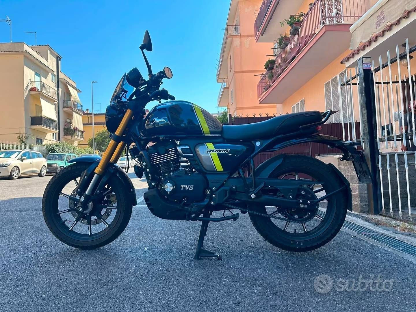 Una motocicletta Yamaha TFX nera è parcheggiata in strada, accanto ad alcuni edifici e a un cancello.