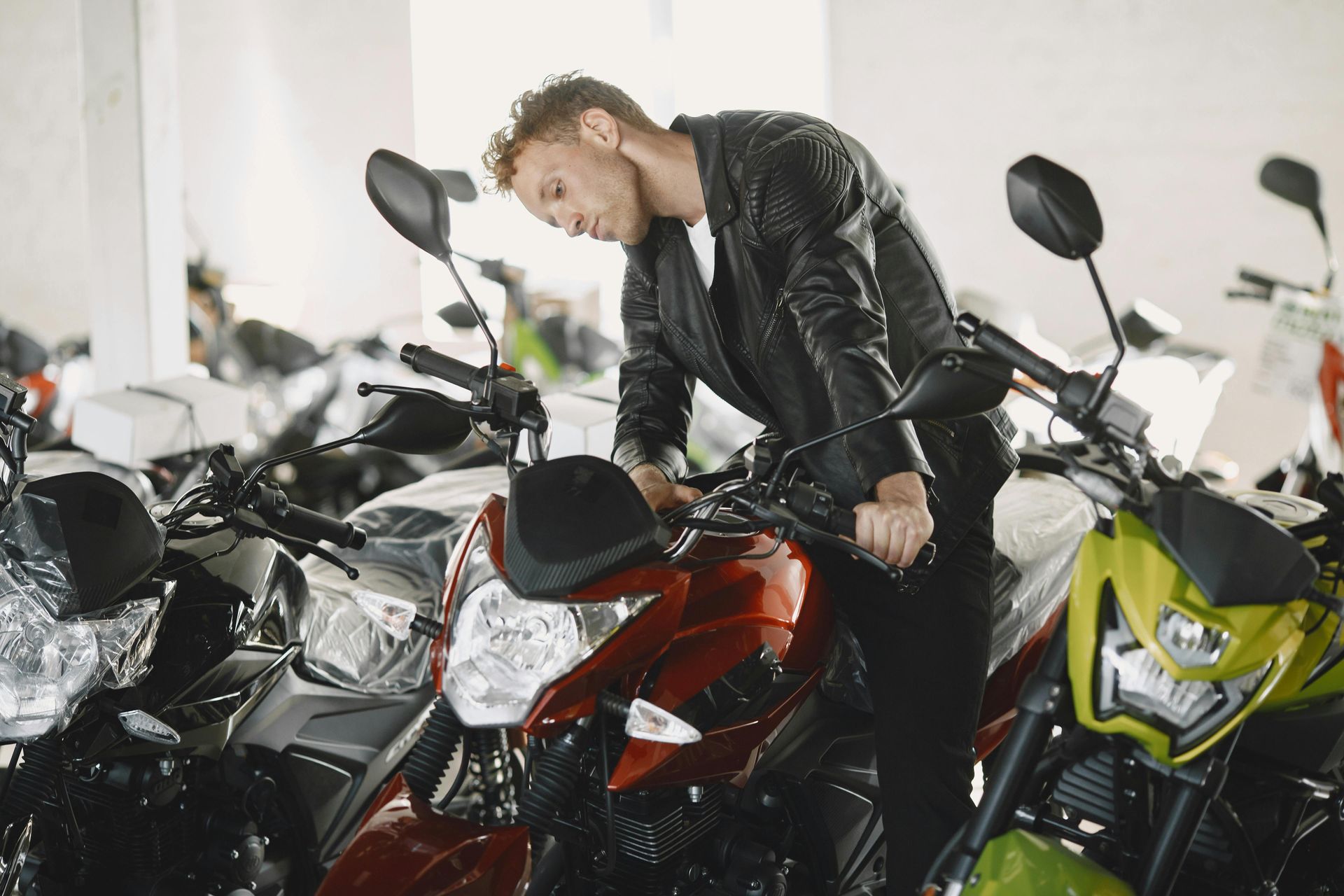 In una concessionaria piena di motociclette di vario tipo, una persona con una giacca di pelle